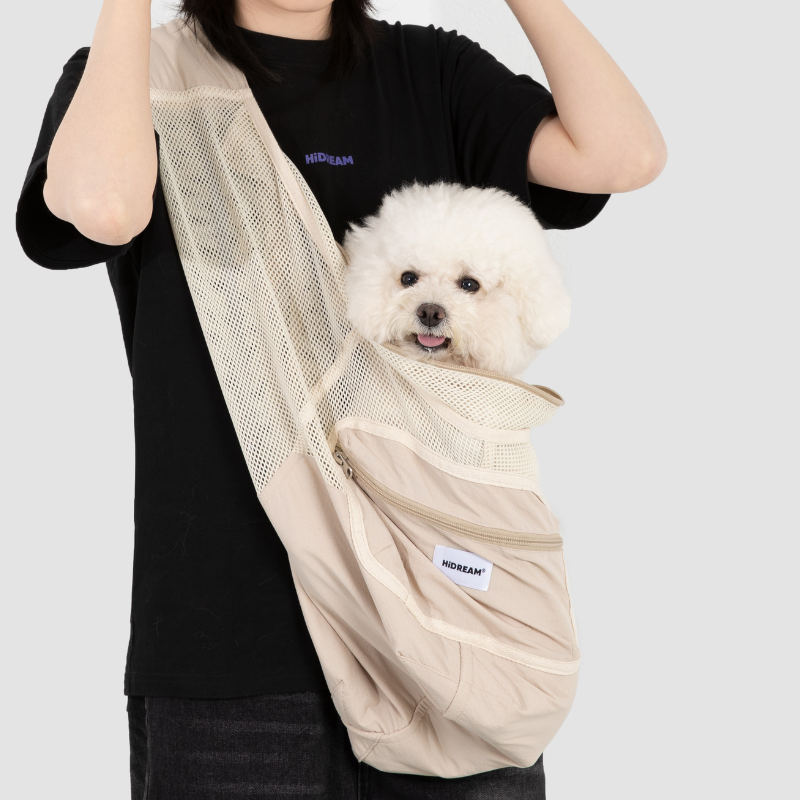Beige urbanTrail breathable pet carrier sling bag with mesh, carrying a small white dog for comfortable travel.