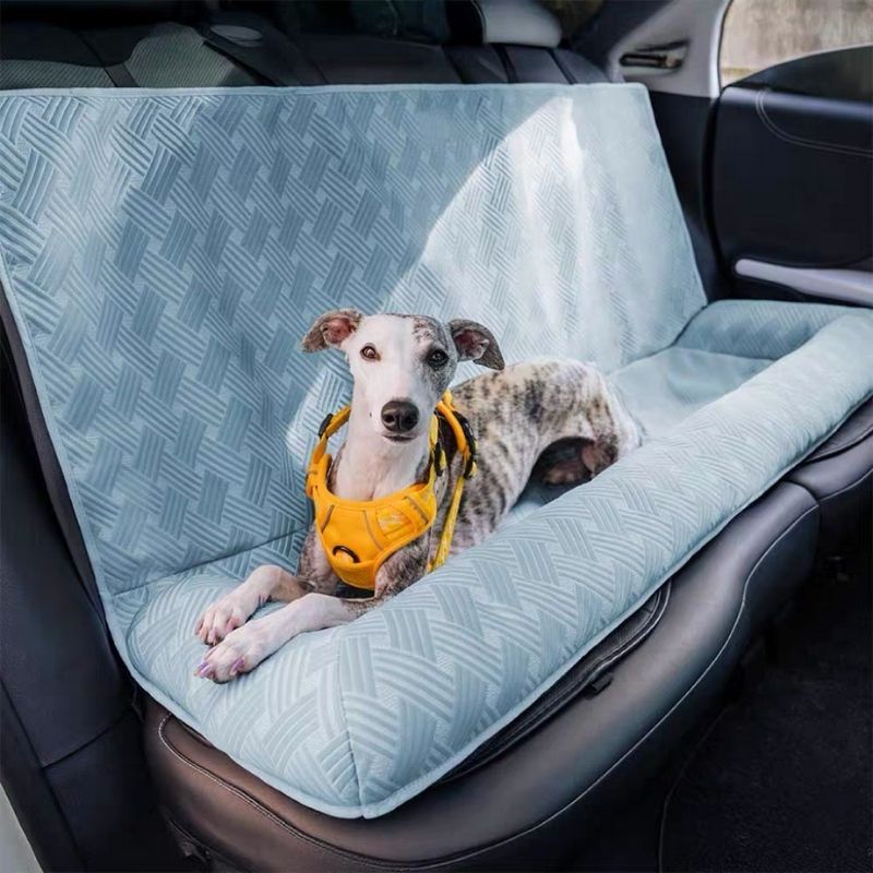 Dog sitting on a car seat cover with a geometric pattern in a vehicle.